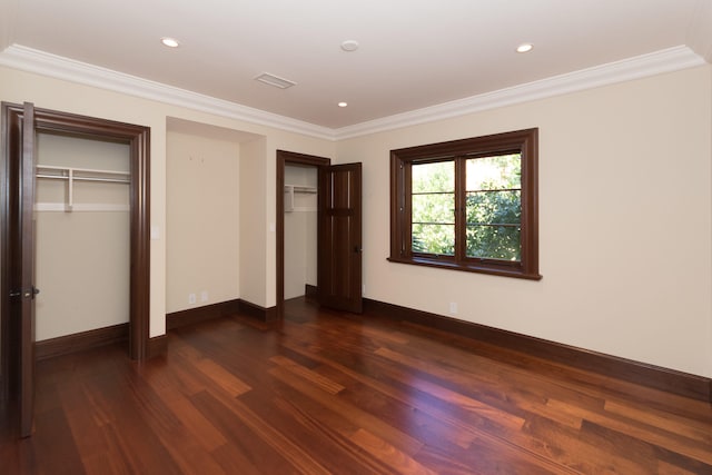 unfurnished bedroom with ornamental molding, dark hardwood / wood-style floors, and two closets