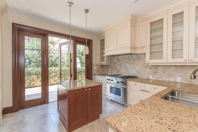 kitchen featuring tasteful backsplash, sink, hanging light fixtures, high end stainless steel range, and cream cabinets