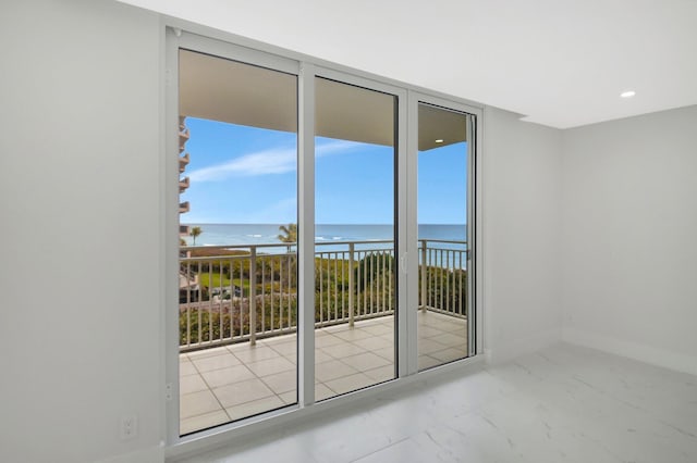 unfurnished room featuring marble finish floor, recessed lighting, a water view, a wall of windows, and baseboards