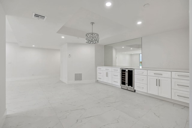 bar featuring a raised ceiling, hanging light fixtures, white cabinets, and wine cooler