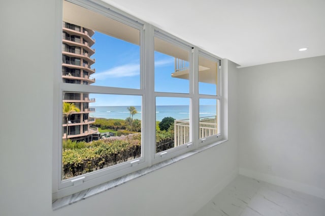 spare room with a water view, marble finish floor, and baseboards