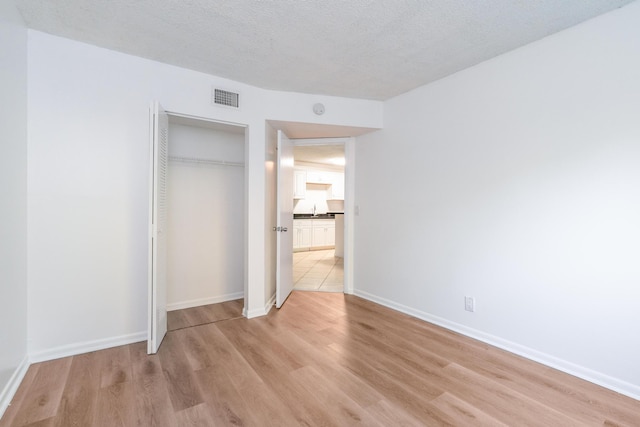 unfurnished bedroom featuring light hardwood / wood-style floors, sink, a textured ceiling, and a closet