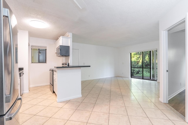 kitchen with white cabinetry, kitchen peninsula, a textured ceiling, light tile patterned floors, and appliances with stainless steel finishes