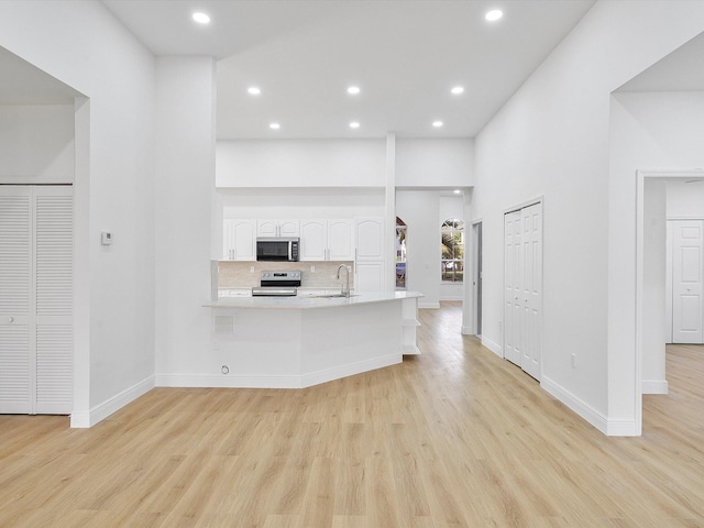 kitchen with stainless steel electric range oven, sink, kitchen peninsula, light hardwood / wood-style floors, and white cabinets