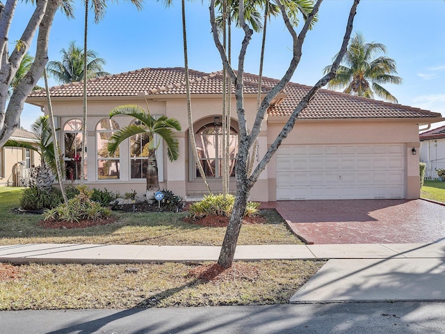 mediterranean / spanish-style home with a tiled roof, decorative driveway, a garage, and stucco siding