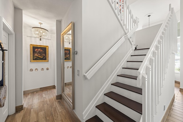 stairway featuring wood-type flooring, a textured ceiling, and a notable chandelier