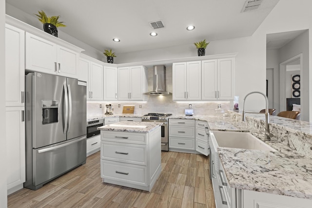 kitchen with appliances with stainless steel finishes, light stone counters, white cabinetry, and wall chimney range hood