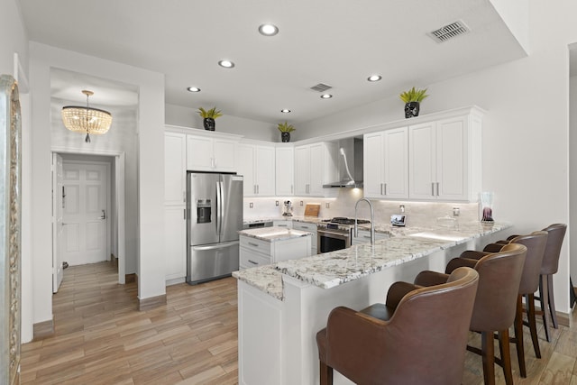 kitchen featuring wall chimney exhaust hood, white cabinetry, stainless steel appliances, and kitchen peninsula