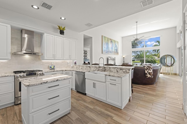 kitchen featuring sink, wall chimney exhaust hood, stainless steel appliances, a kitchen island, and white cabinets