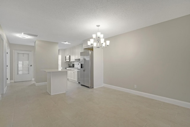 kitchen with appliances with stainless steel finishes, backsplash, pendant lighting, white cabinets, and a chandelier