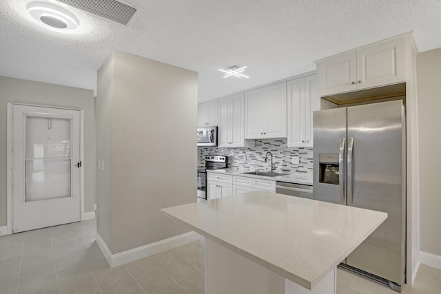 kitchen featuring a textured ceiling, stainless steel appliances, sink, white cabinets, and a kitchen island