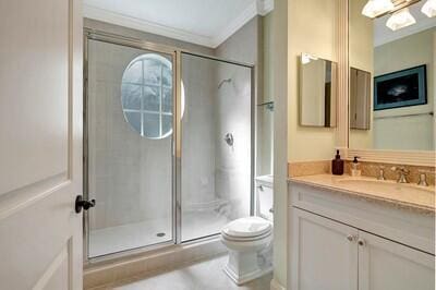 bathroom featuring toilet, a shower with door, vanity, and ornamental molding