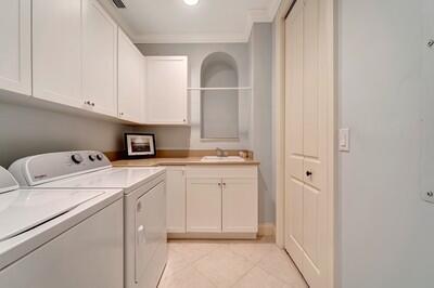 laundry room featuring cabinets, crown molding, sink, light tile patterned floors, and independent washer and dryer