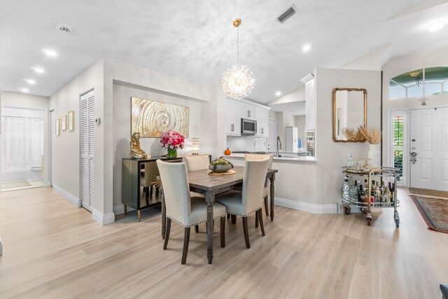 dining room featuring a notable chandelier, light wood-type flooring, sink, and vaulted ceiling