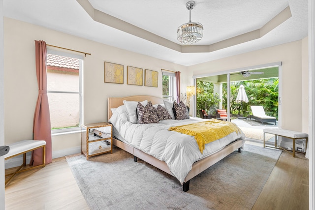 bedroom with a raised ceiling, a chandelier, a textured ceiling, access to outside, and light wood-type flooring