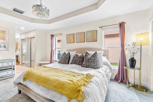 bedroom with a tray ceiling, a closet, light hardwood / wood-style floors, and a notable chandelier