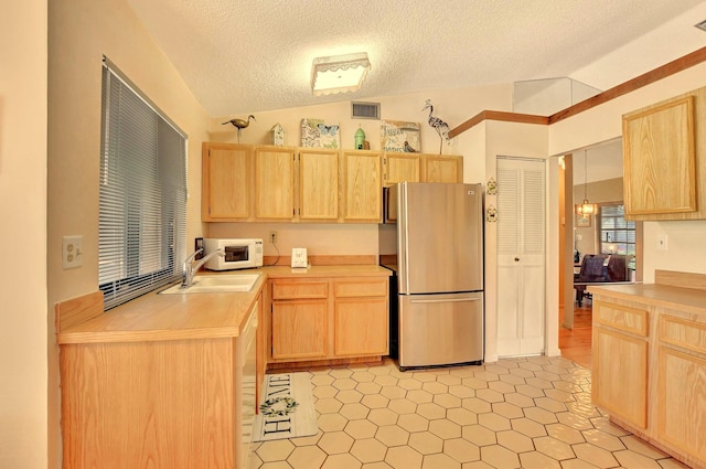 kitchen with stainless steel refrigerator, light brown cabinetry, and vaulted ceiling