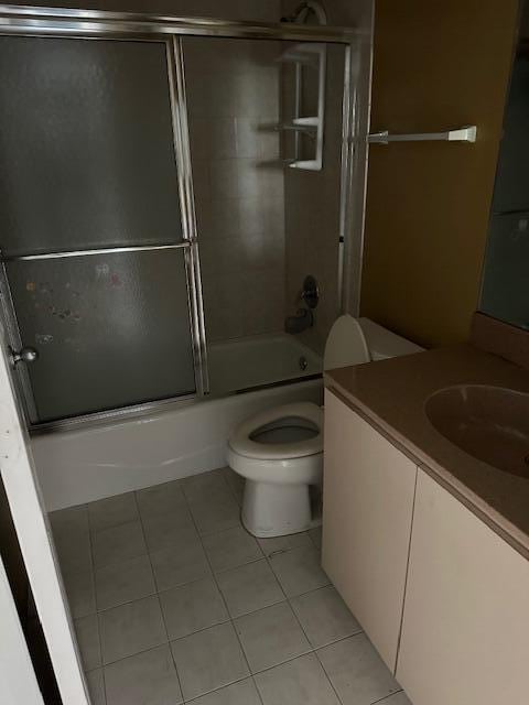 full bathroom featuring combined bath / shower with glass door, vanity, tile patterned flooring, and toilet