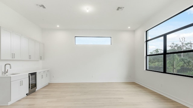 bar featuring white cabinets, light hardwood / wood-style floors, beverage cooler, and sink