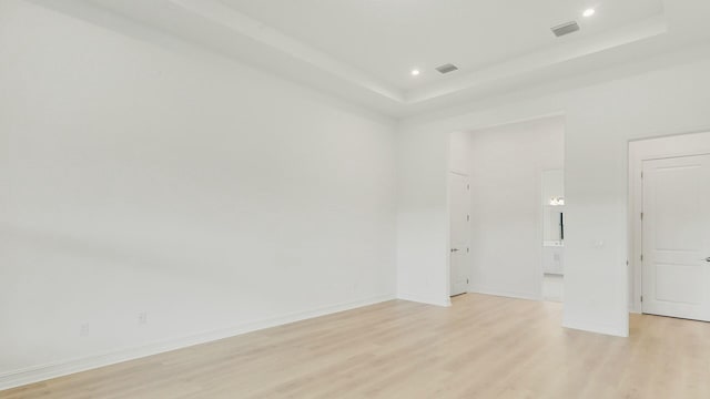 spare room with light hardwood / wood-style flooring and a raised ceiling