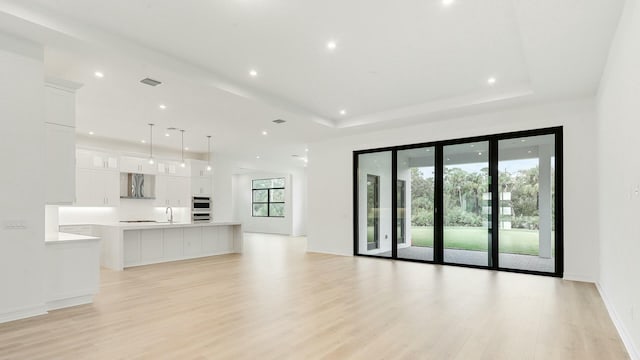 unfurnished living room featuring a tray ceiling, a wealth of natural light, sink, and light wood-type flooring