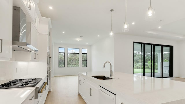 kitchen with pendant lighting, sink, wall chimney exhaust hood, appliances with stainless steel finishes, and white cabinetry