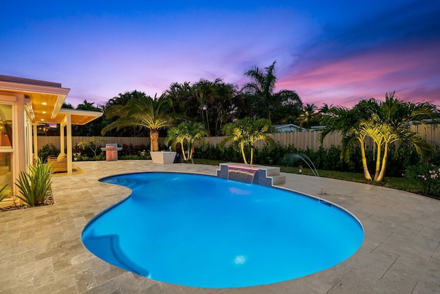 pool at dusk with pool water feature, a grill, and a patio