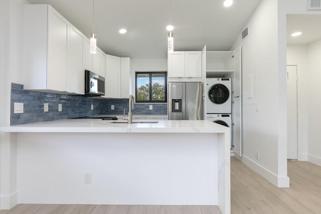 kitchen featuring appliances with stainless steel finishes, white cabinetry, hanging light fixtures, and stacked washer and clothes dryer