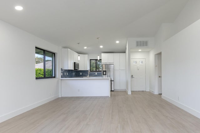 interior space with white cabinets, light wood-type flooring, appliances with stainless steel finishes, decorative light fixtures, and kitchen peninsula