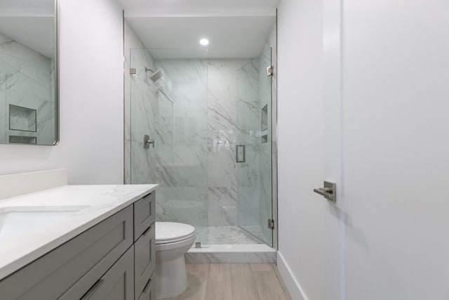 bathroom featuring a shower with door, vanity, and toilet