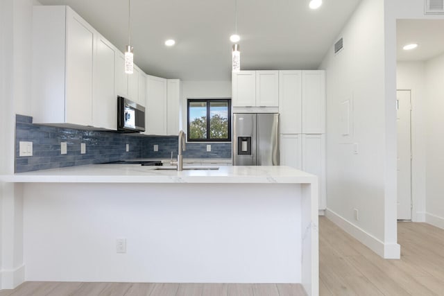 kitchen featuring white cabinets, appliances with stainless steel finishes, light wood-type flooring, and pendant lighting