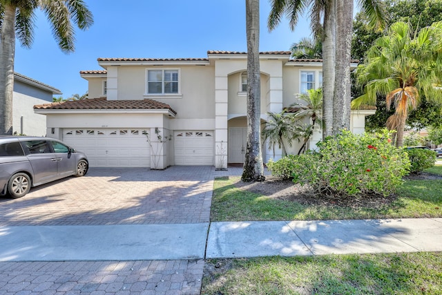 mediterranean / spanish-style house featuring stucco siding, a tiled roof, an attached garage, and decorative driveway