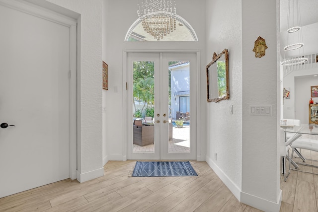 foyer entrance featuring french doors, a notable chandelier, wood finished floors, and a textured wall