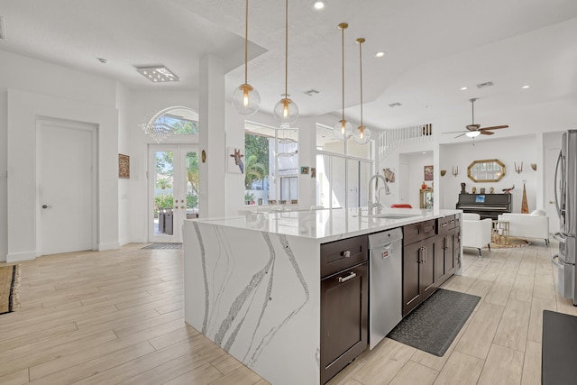 kitchen with a center island with sink, wood finish floors, a sink, stainless steel appliances, and dark brown cabinets