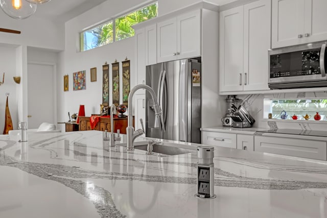 kitchen featuring tasteful backsplash, white cabinets, appliances with stainless steel finishes, and light stone countertops