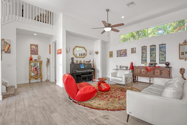 living room featuring wood finished floors, visible vents, a towering ceiling, and ceiling fan