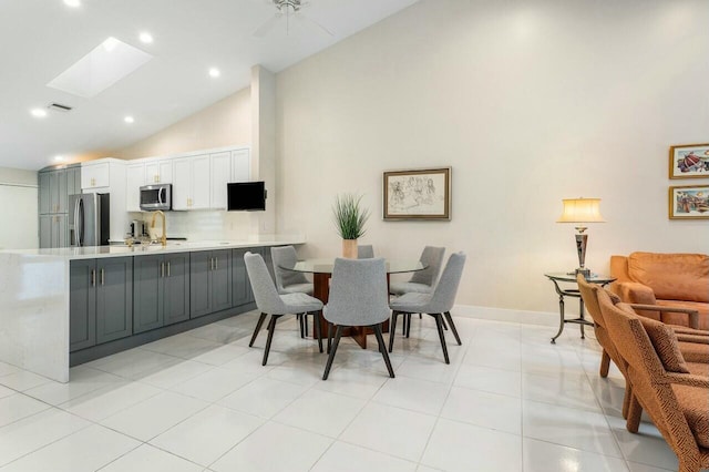 tiled dining space featuring ceiling fan, high vaulted ceiling, and a skylight