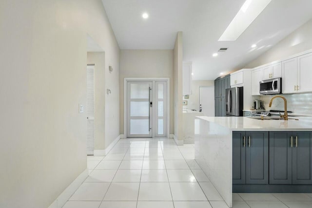 kitchen with a skylight, stainless steel appliances, sink, white cabinets, and light tile patterned flooring