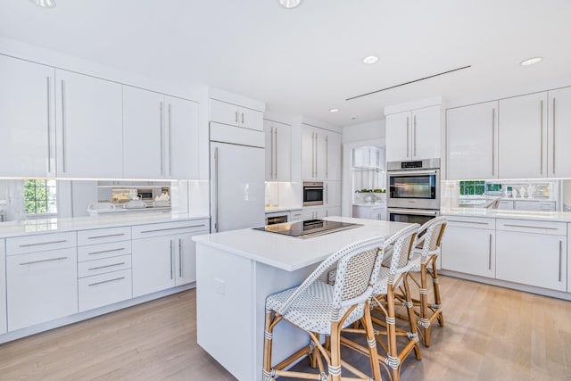 kitchen with double oven, black electric stovetop, built in fridge, white cabinetry, and light countertops