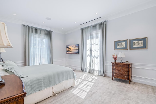 bedroom with wainscoting, a decorative wall, crown molding, and light colored carpet