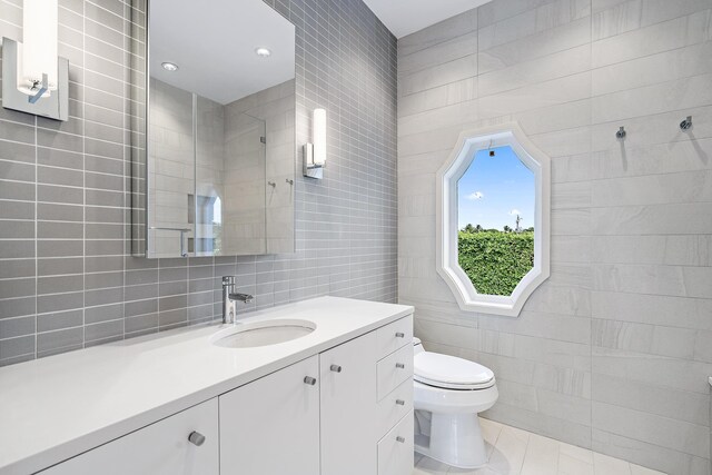 bathroom featuring tile walls, toilet, vanity, tile patterned flooring, and tiled shower