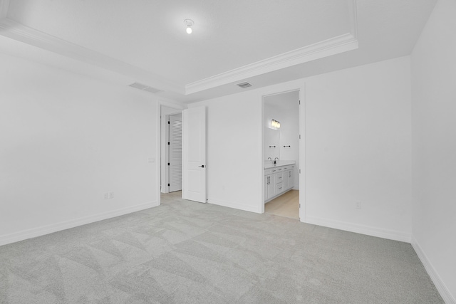 unfurnished bedroom featuring light carpet, ornamental molding, ensuite bathroom, and a tray ceiling