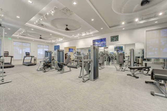 gym featuring a tray ceiling, ceiling fan, and light colored carpet