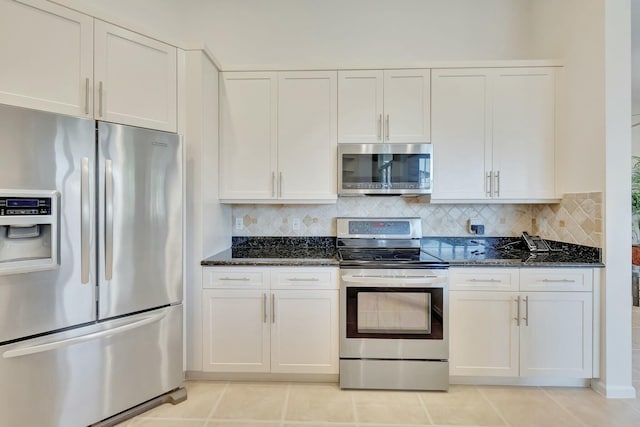 kitchen featuring backsplash, dark stone counters, stainless steel appliances, white cabinetry, and light tile patterned flooring