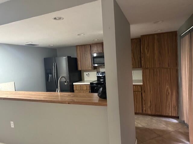 kitchen featuring kitchen peninsula, sink, refrigerator with ice dispenser, light tile patterned floors, and black electric range