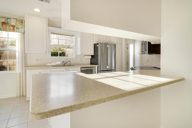 kitchen with kitchen peninsula, stainless steel appliances, sink, white cabinetry, and light tile patterned flooring