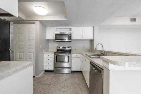 kitchen featuring white cabinets, appliances with stainless steel finishes, sink, light tile patterned floors, and a tray ceiling