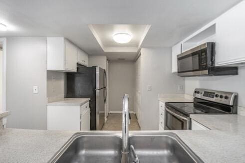 kitchen featuring a raised ceiling, white cabinets, appliances with stainless steel finishes, and sink