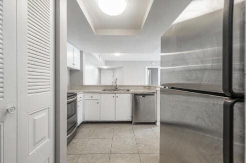 kitchen featuring light tile patterned flooring, stainless steel appliances, white cabinets, and a tray ceiling