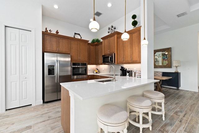 kitchen with light wood-type flooring, stainless steel appliances, sink, decorative light fixtures, and a breakfast bar area